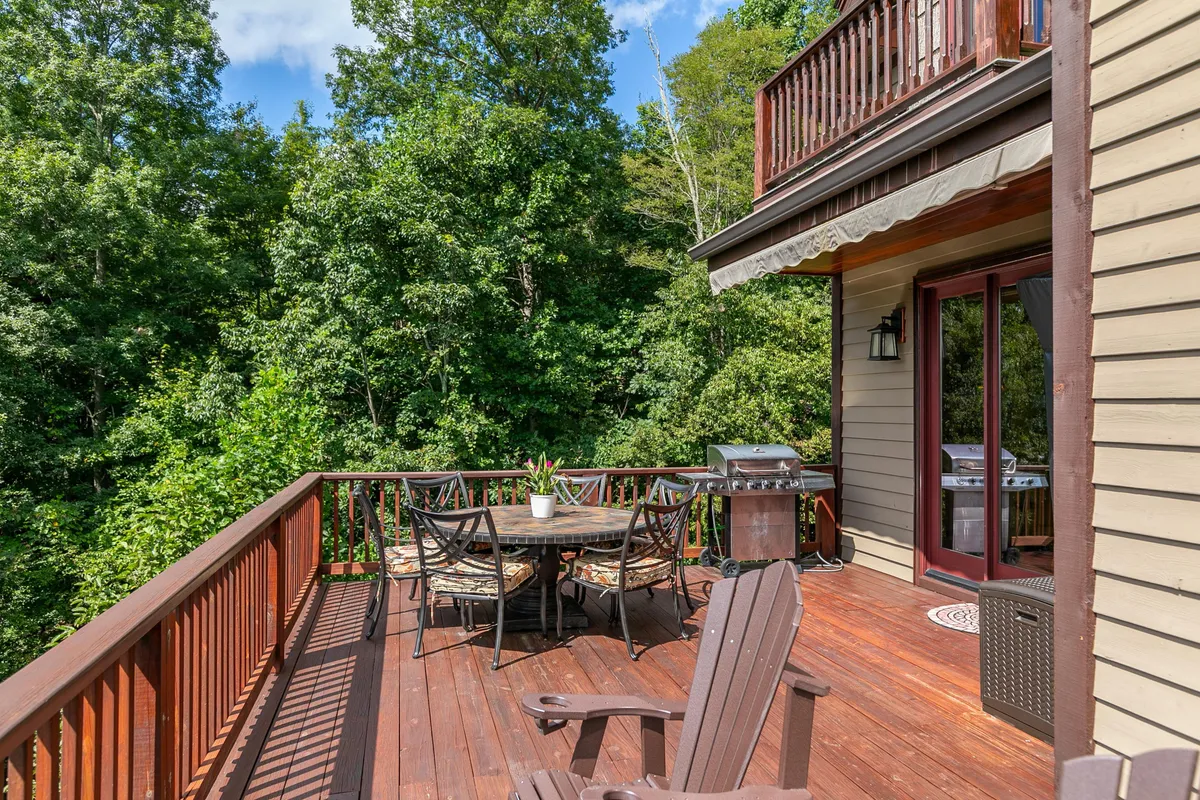 A spacious outdoor deck with an elegant dining setup, grill, and comfortable seating, all set amid vibrant green foliage. The scene is inviting for social gatherings, outdoor meals, and moments of relaxation in nature.