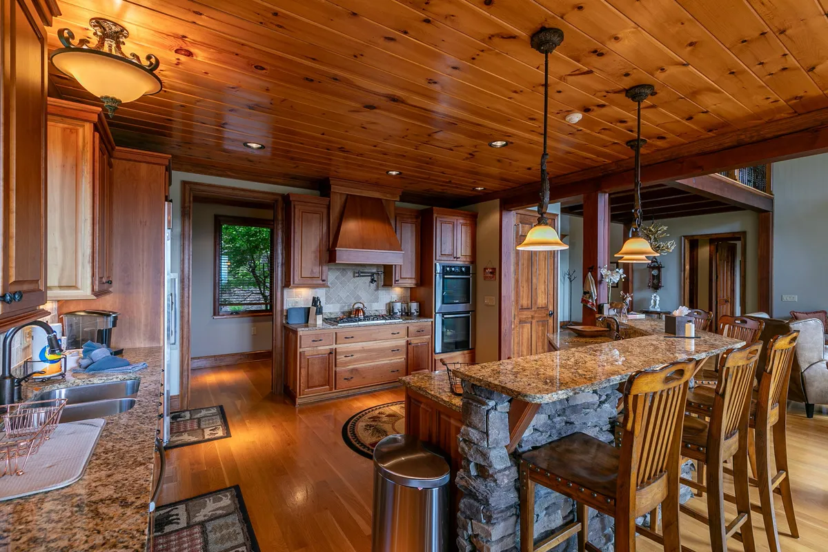 A cozy, well-appointed kitchen area features a granite-topped island with seating, pendant lighting, wood cabinetry, and modern stainless steel appliances. The open design is perfect for both meal preparation and connecting with guests or family during extended stays.