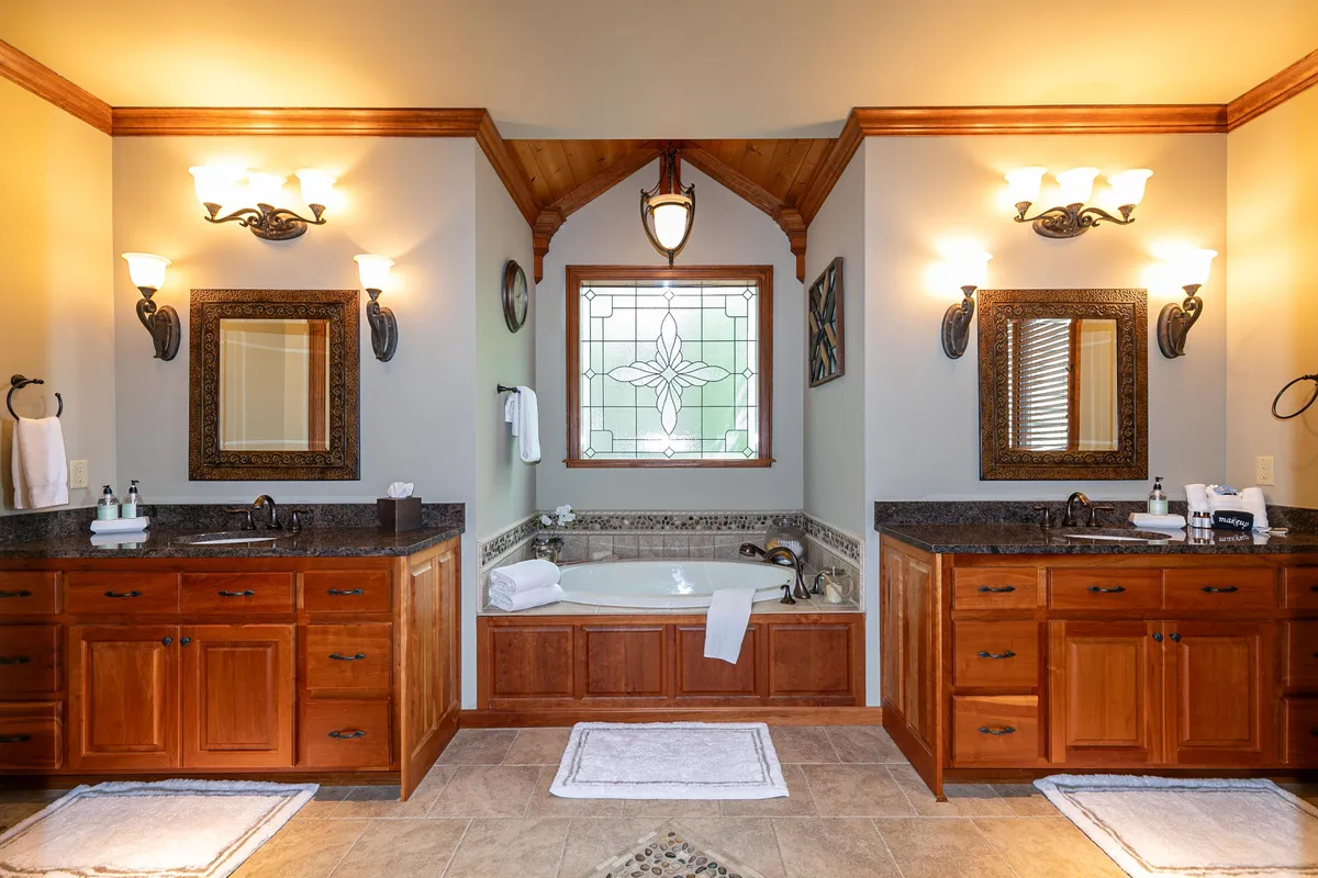 A spacious, serene bathroom with double vanity sinks, a feature stained glass window casting soft light, and a luxurious bathtub. The decor is elegant and soothing, inviting relaxation and providing a sense of a private spa experience.
