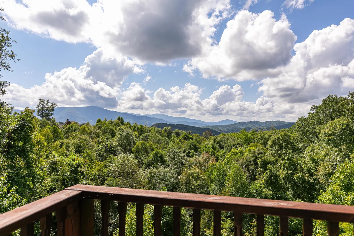 A sweeping view of the Blue Ridge mountain range, dense forests, and a sky filled with soft clouds. The vantage point is from a balcony or outdoor perch, immersing the viewer in the beauty and tranquility of nature that surrounds Headwaters at Banner Elk.