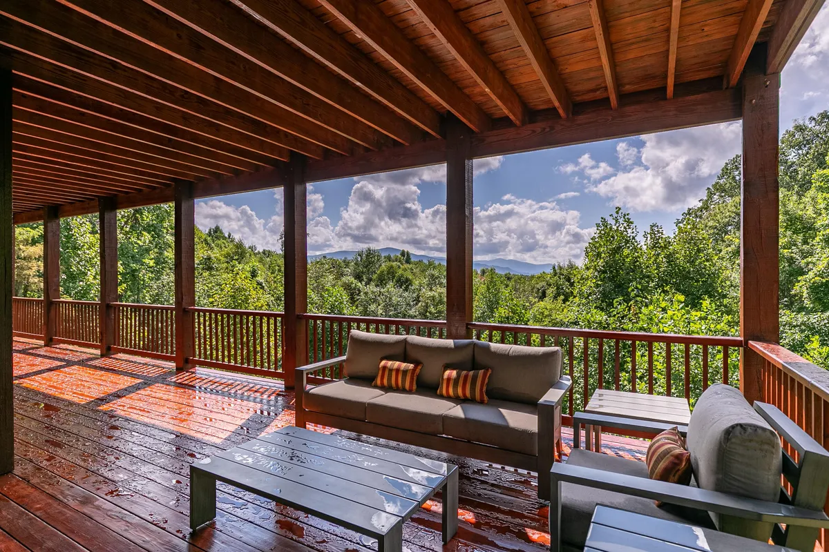 A spacious deck furnished with comfortable seating, offering panoramic views of the surrounding natural landscape. The space invites relaxation, morning coffee, or stargazing, with the backdrop of forests and mountains visible beyond the railing.