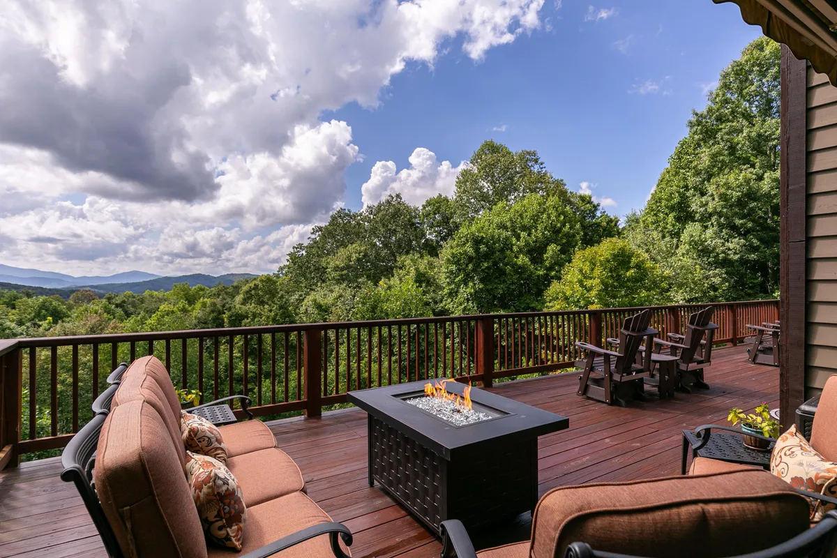 An expansive outdoor patio with comfortable seating gathered around a glowing fire pit, surrounded by lush greenery and a scenic mountain backdrop, ideal for relaxation, outdoor dining, and stargazing under open skies.